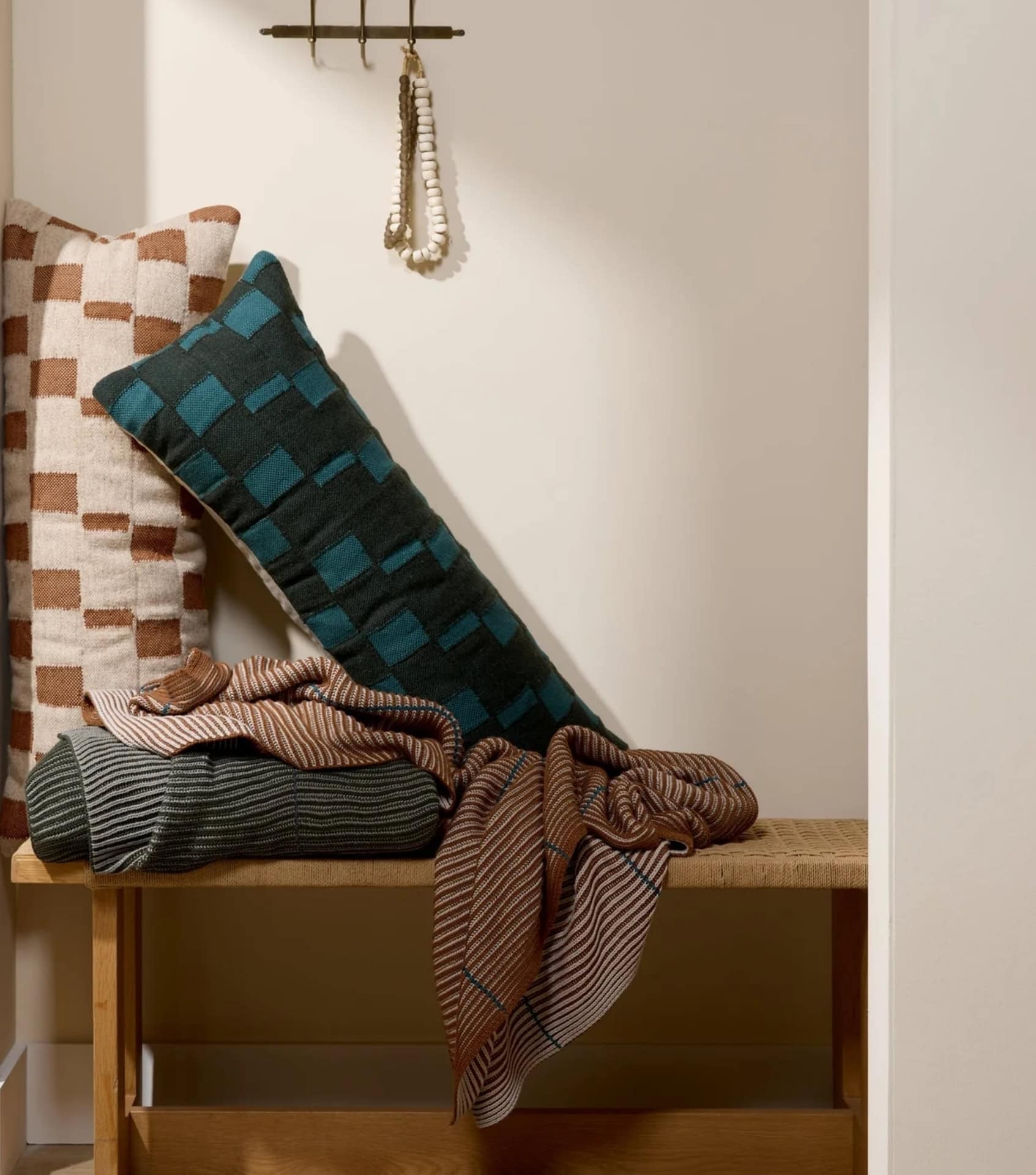 Sustainable homewares including patterned throw pillows, blankets, and natural wood bench with artisan textiles