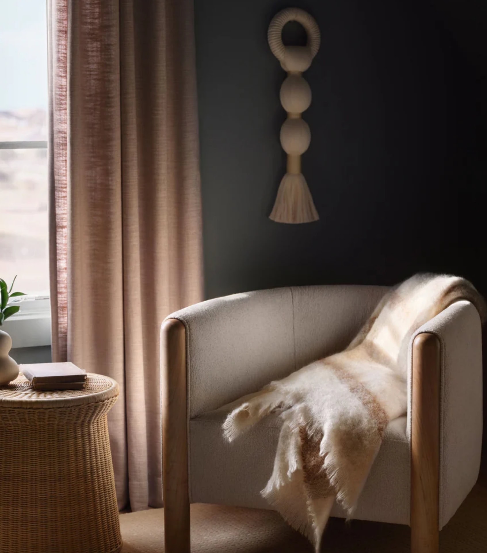 Sustainable home goods featuring a neutral armchair with sheepskin throw, woven side table, and natural fiber wall hanging. By The Citizenry