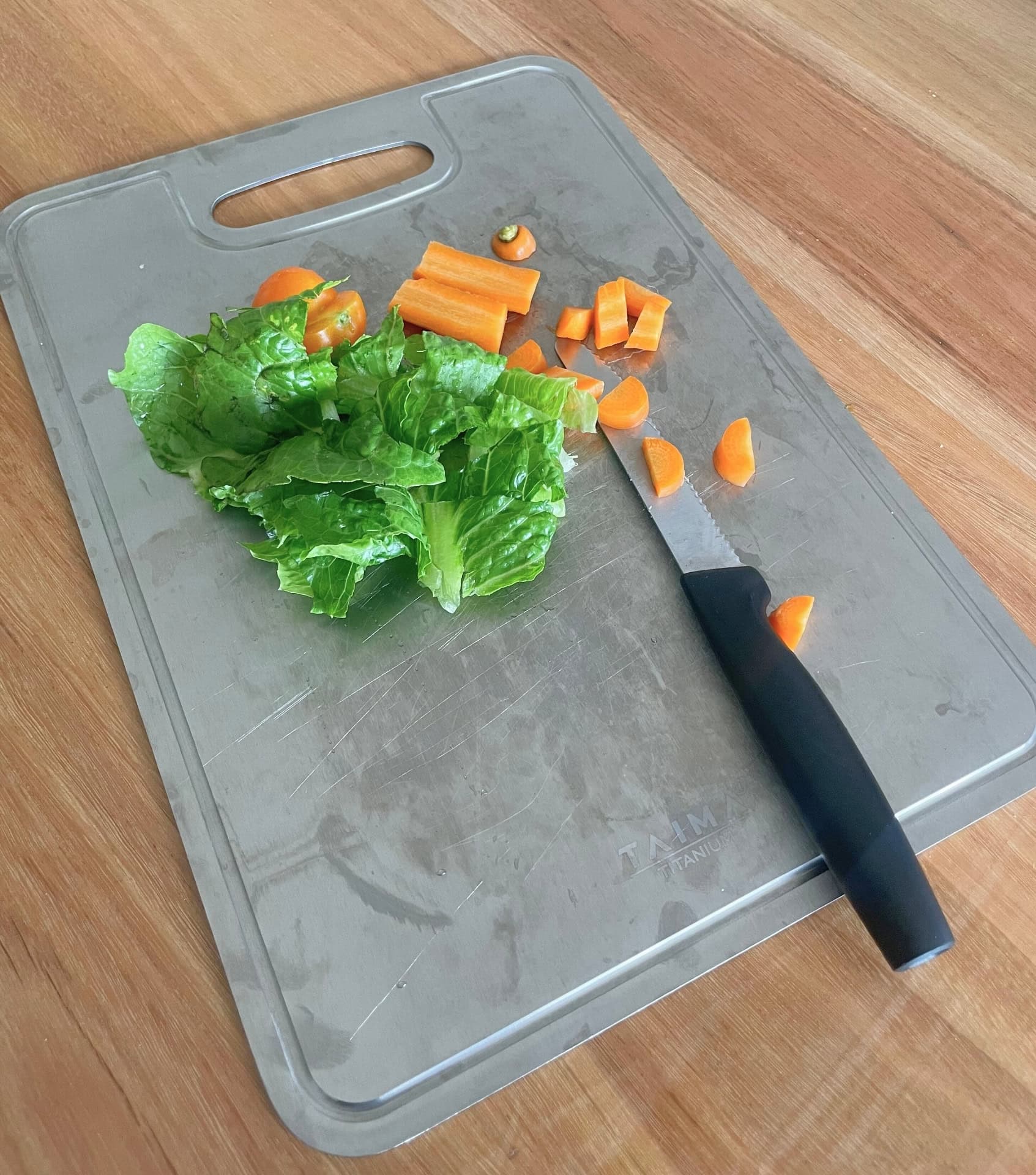 Taima titanium cutting board being tested with fresh vegetables showing non-toxic food-grade metal surface